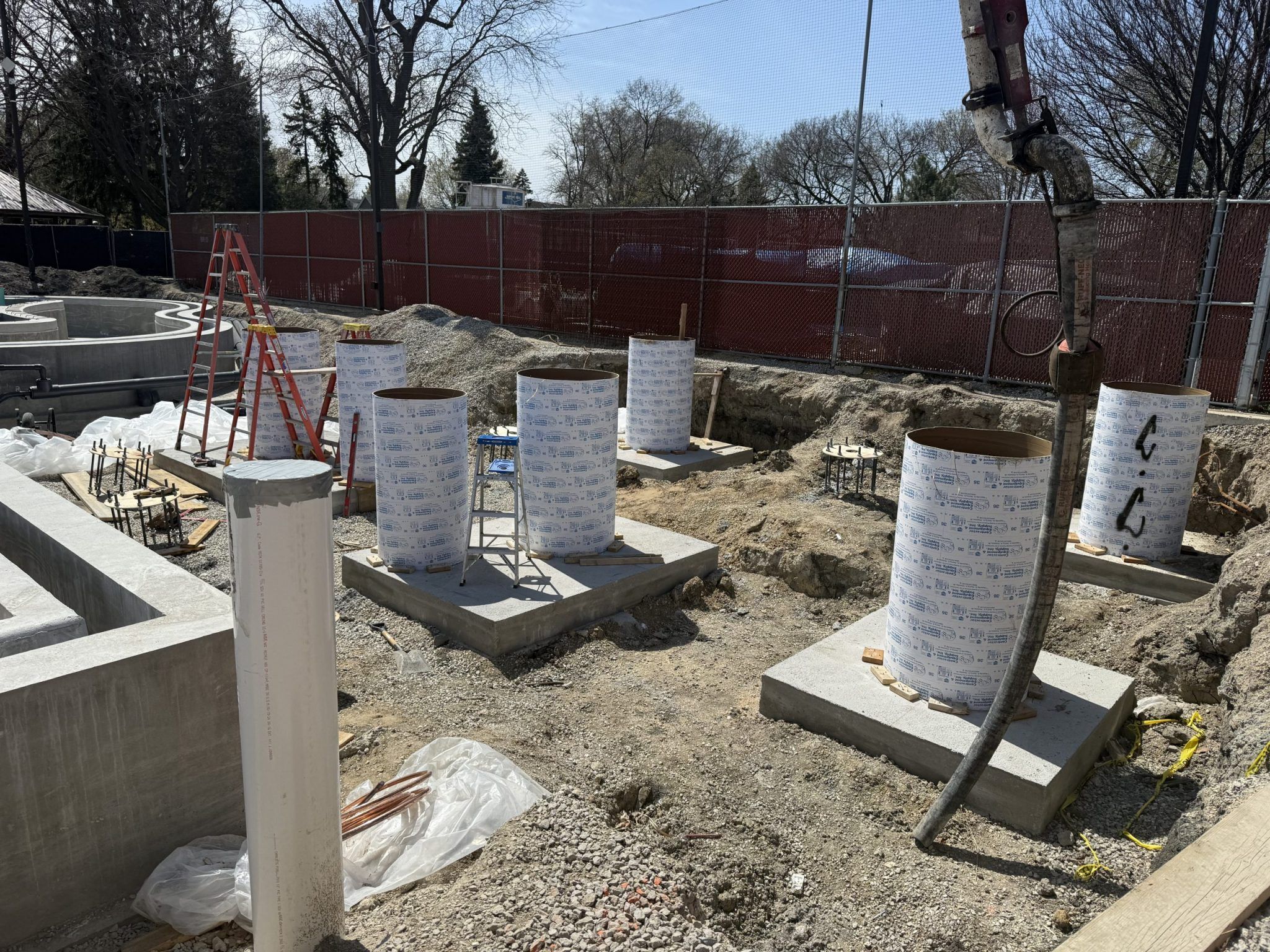 Construction site at Rehm Park & Pool with concrete forms for pillars and a concrete pump hose.