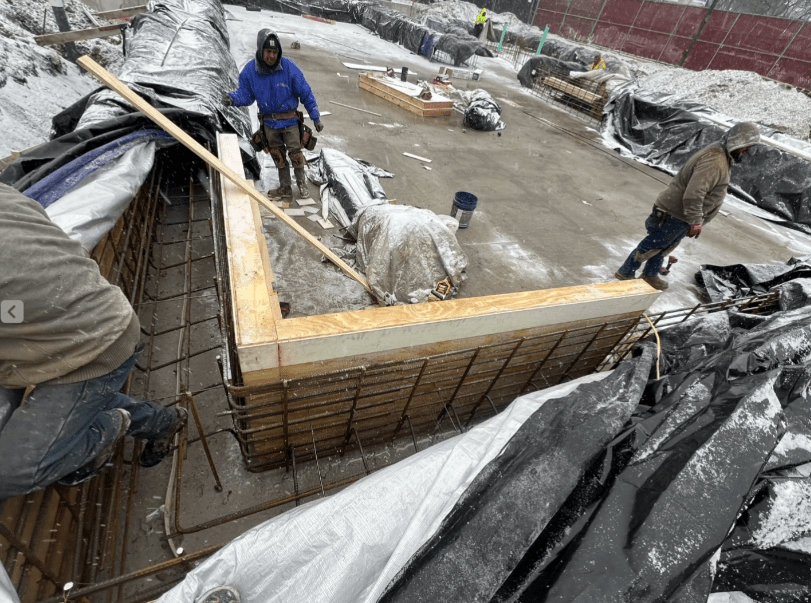 Construction workers in winter conditions building a pool foundation with rebar and wooden forms at Rehm Park & Pool.