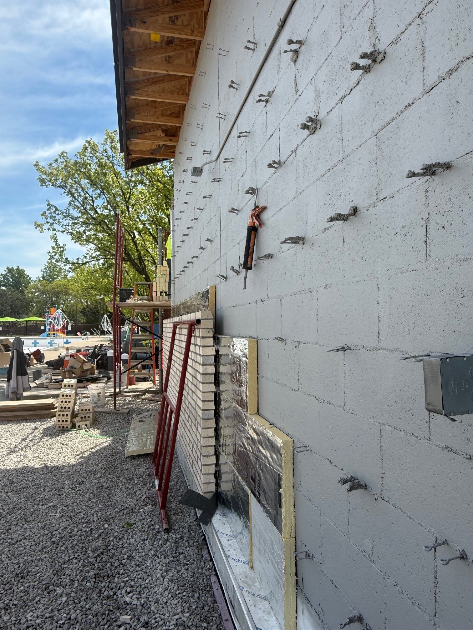 Construction of Rehm Park & Pool exterior wall with insulation and brick veneer in progress. Metal ties protrude from cinder