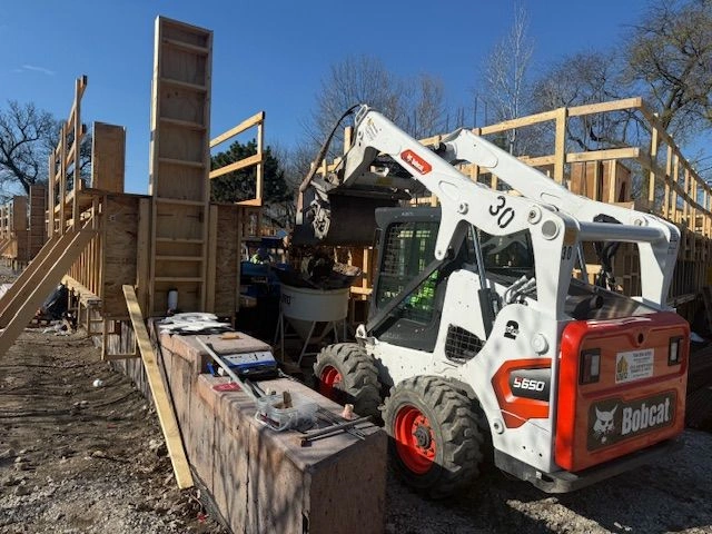 A white Bobcat S650 skid-steer loader is positioned next to wooden formwork for a concrete structure at the Field Park