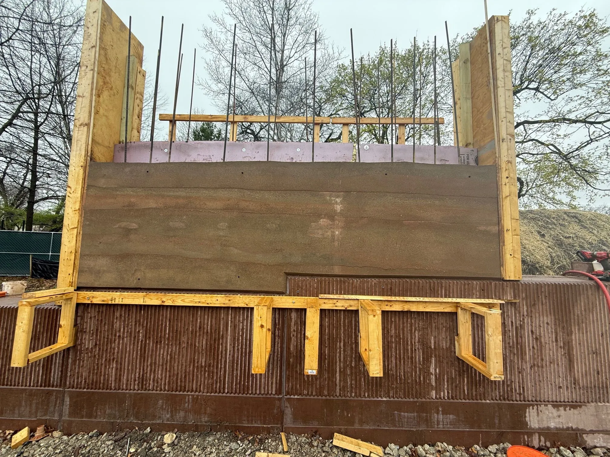 Construction of a rammed earth wall at Field Park, showing wooden formwork, rebar, insulation, and the layered earth.