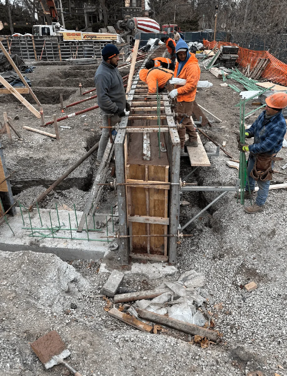 Construction workers pour concrete into forms at the Field Park construction site. Rebar is visible.
