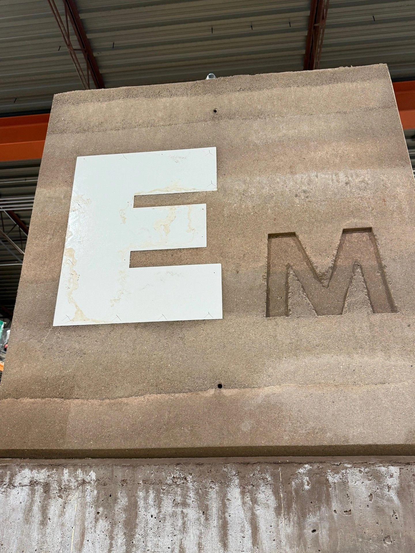 A concrete structure with the letters "E" and "M" displayed. The "E" is a white cutout, and the "M" is carved into the