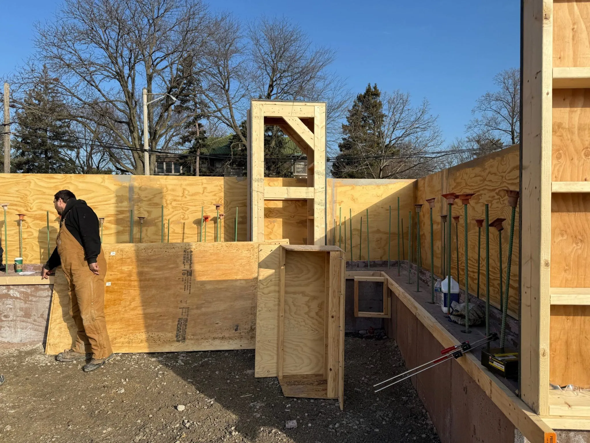 Construction worker in overalls inspects plywood formwork for a concrete foundation at Field Park.
