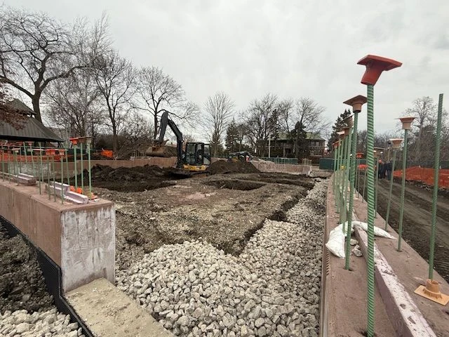Construction site at Field Park with an excavator digging in the dirt and rebar sticking out of concrete walls.