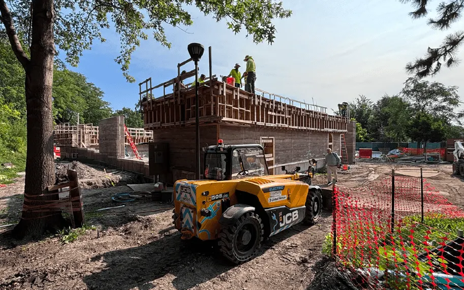 Construction of Field Park building with workers and a yellow JCB telehandler.