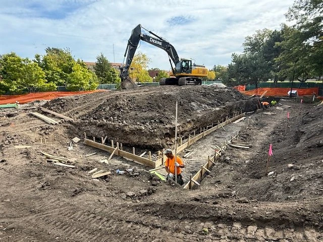 Construction workers and an excavator are on site at Field Park, preparing the foundation for a new building.