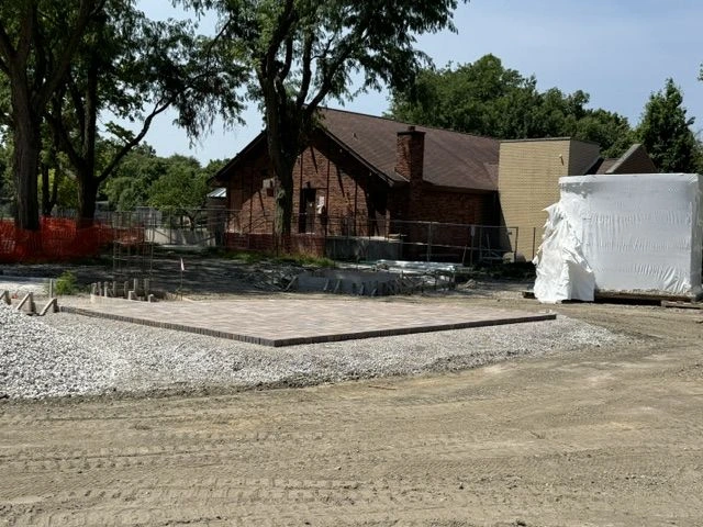 Construction of a paved patio area at Longfellow Park, with a brick building and materials in the background.