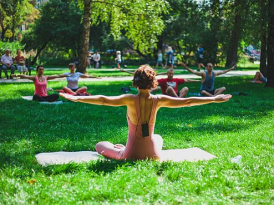 A group of people practice yoga outdoors in a park, led by an instructor in the foreground.
