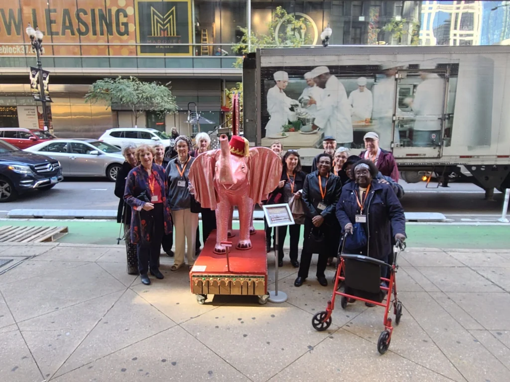 A group of people pose with a pink elephant statue on a red platform in front of a truck with a chef mural.