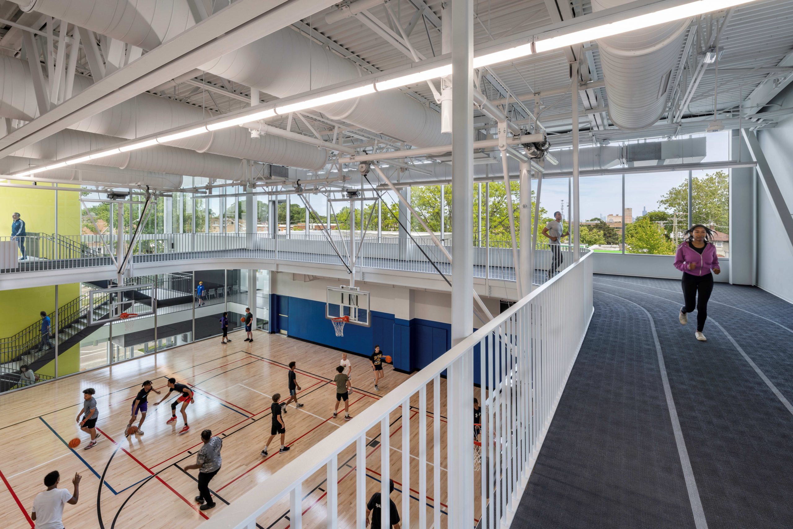People playing basketball on a wooden court and a woman running on an indoor track in a modern gymnasium.