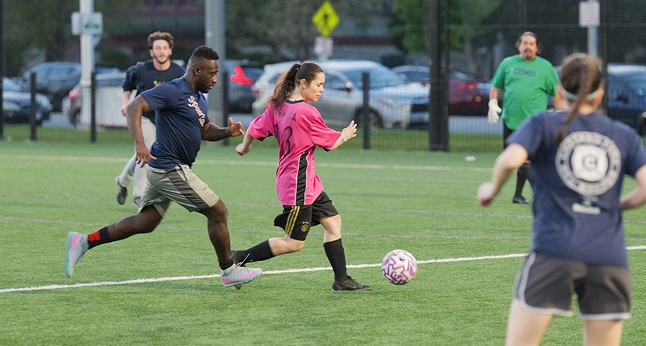 A man and woman playing soccer on a field. The woman in pink is kicking the ball.
