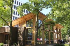 Austin Gardens building with large glass windows and wooden exterior, surrounded by trees.