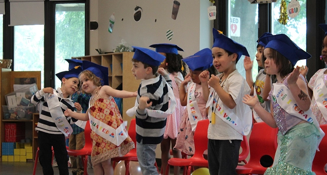 Preschool children in graduation caps and sashes celebrate their graduation.