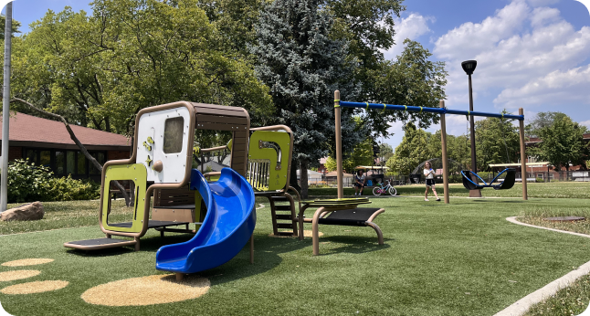 Modern playground with a blue slide, swings, and climbing structure on artificial turf.