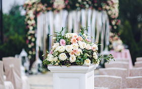 Floral arrangement on pedestal in front of wedding ceremony arch and seating.