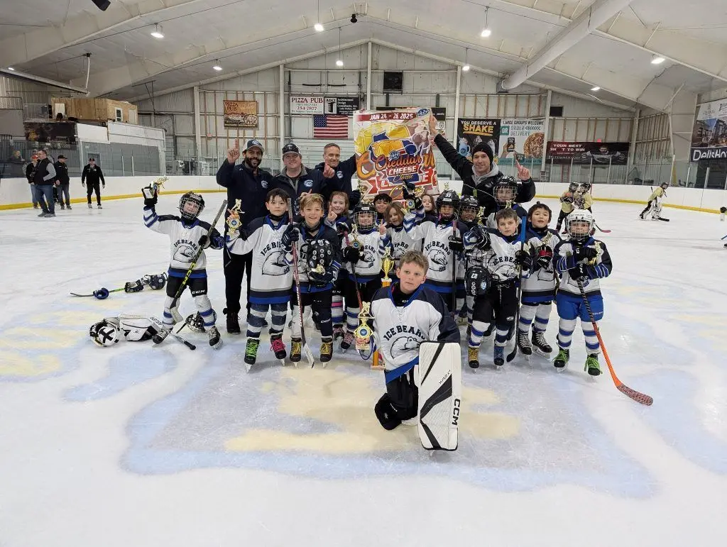 Ice Bears Mite hockey team poses with trophies and coaches on the ice after a game.