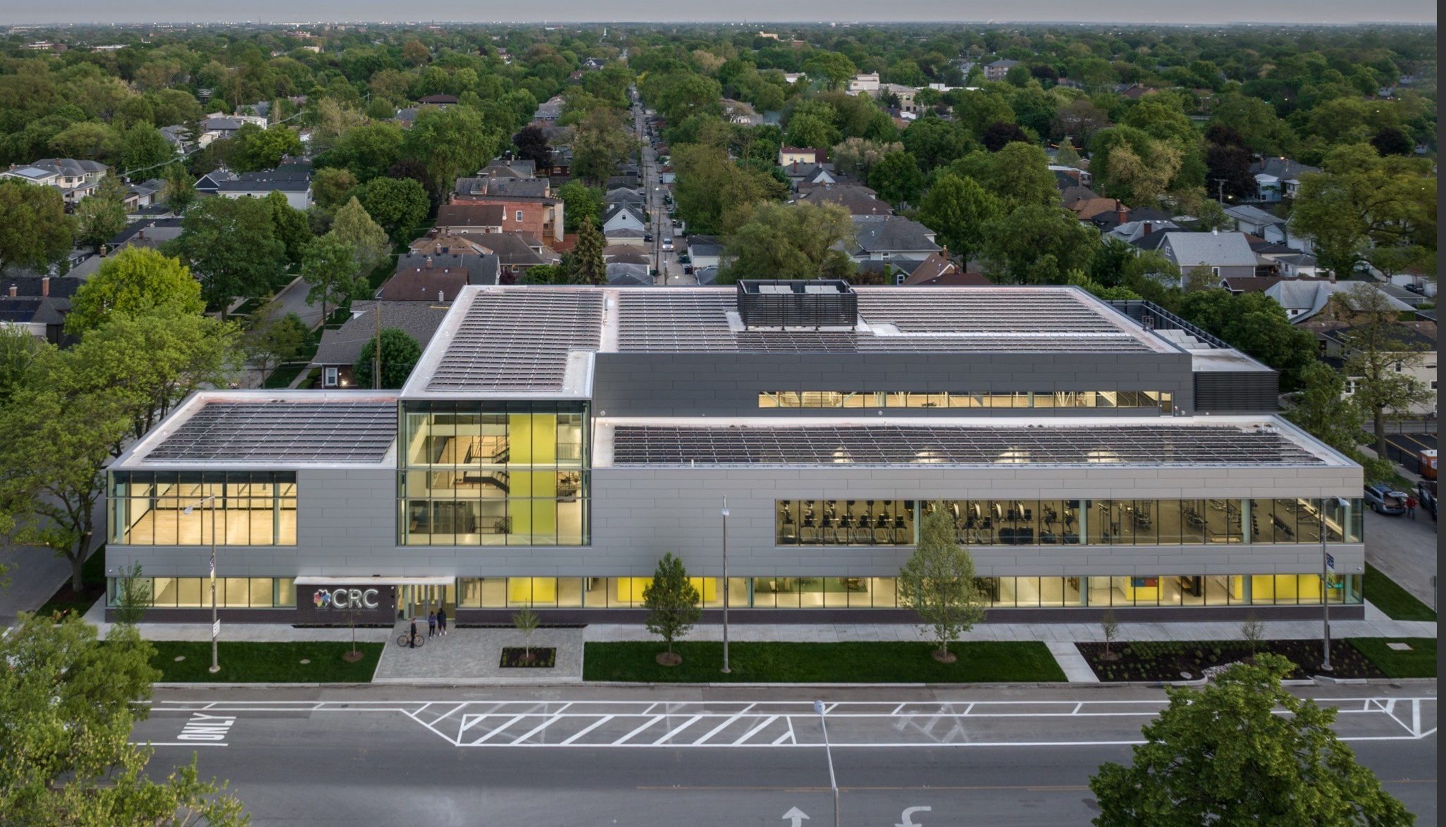 Aerial view of the CRC building, a modern structure with solar panels on the roof and large windows showcasing gym equipment
