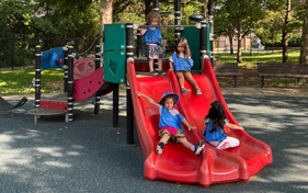 Group of children slide down a red slide.