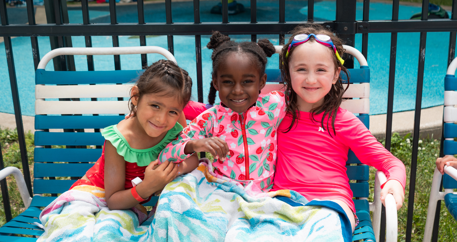 three girls wrapped smile at the camera while sitting on some pool chairs