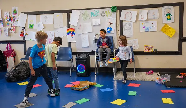 Children engaged in activities during a winter/spring break camp program, with artwork displayed on the wall.