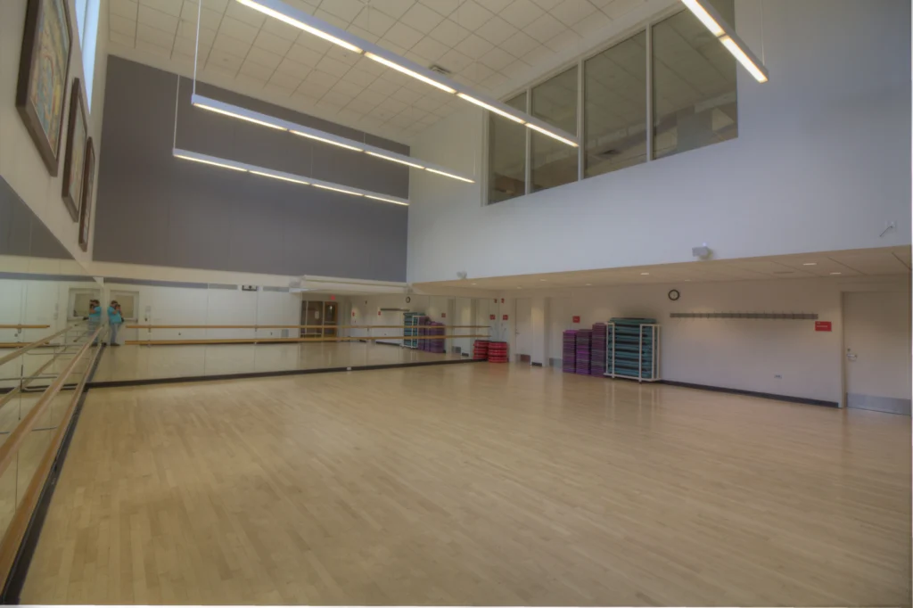 Spacious dance studio with mirrored walls, ballet barres, wooden floor, and stacked aerobic steps.