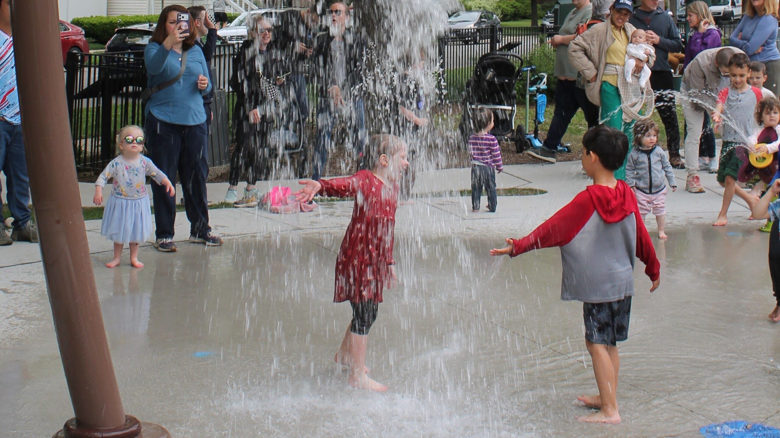 two kids stand under a fountain of water with other splash features in the background