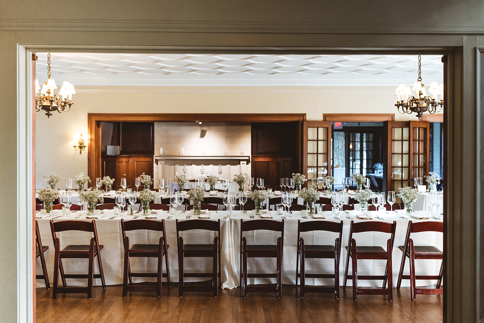 long tables with white table clothes set up in historic room with fireplace and chandeliers