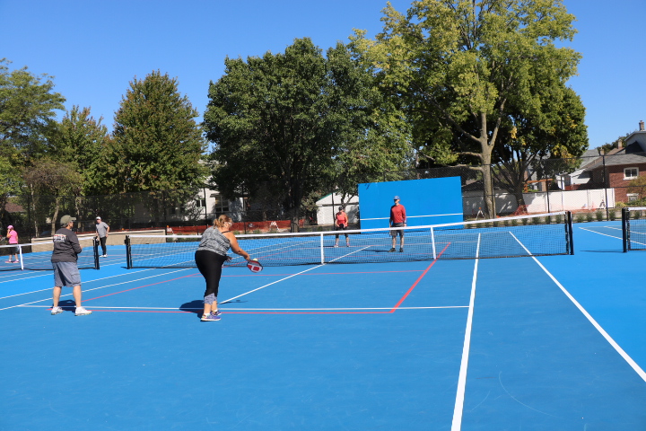 People playing pickleball on a bright blue court with white and red lines under a clear sky.
