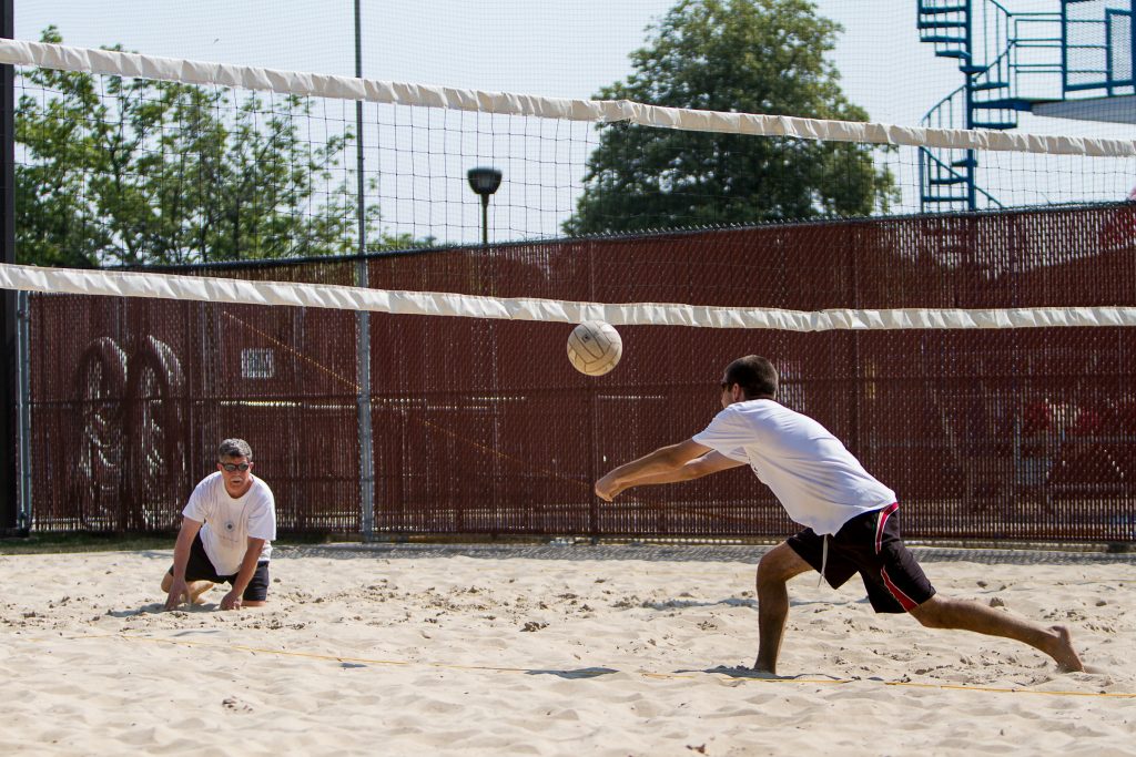 Two men playing beach volleyball on a sand court. One man is in the foreground, lunging to hit the ball over the net.