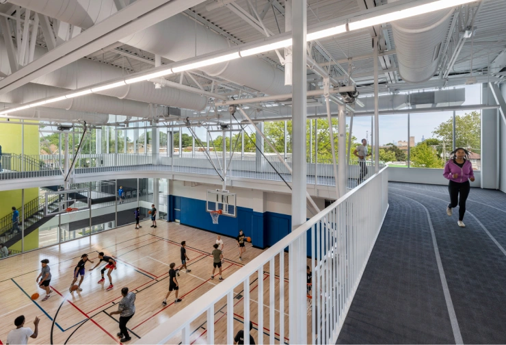 People run on an elevated indoor track overlooking a basketball court where a game is in progress.