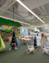 Children playing in a brightly decorated indoor play area with swings, tables, and chairs.