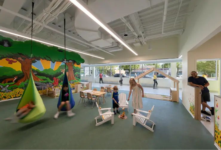 Children enjoy swings and a play campfire in a brightly decorated Playzone Childcare room with a forest mural.