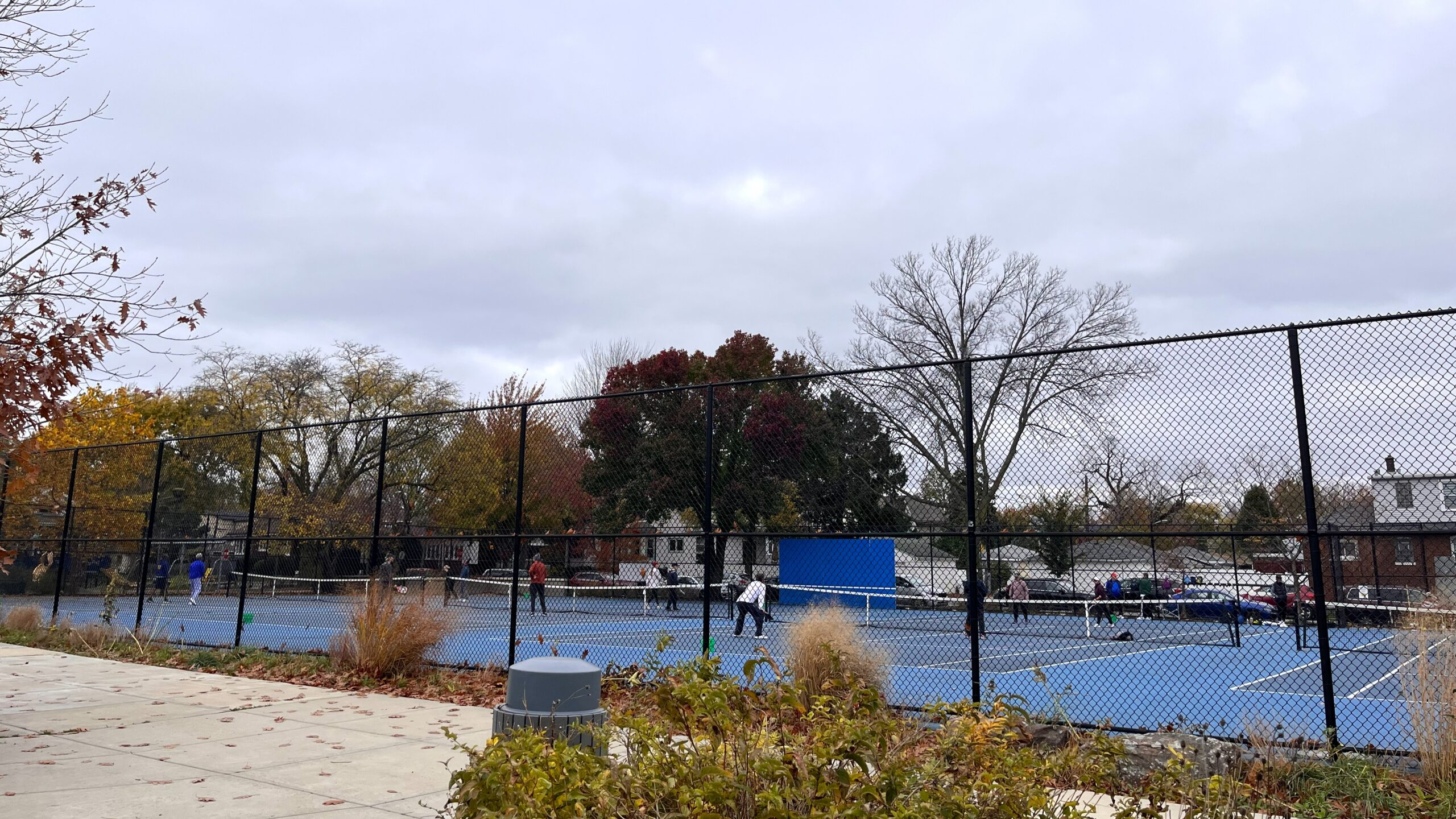 people play on pickleball and tennis courts behind a large fence