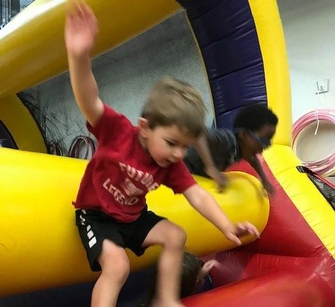 A young boy in a red shirt and black shorts climbs on a yellow and red inflatable structure at the Gymnastics and Recreation