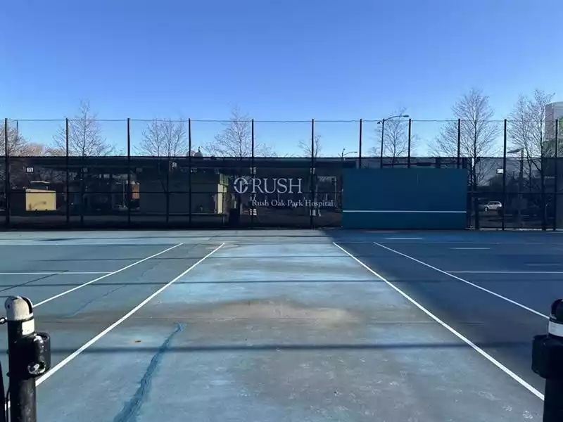 Outdoor tennis court with a banner for Rush Oak Park Hospital in the background.