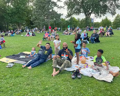 A group of people enjoy a picnic and outdoor event on a grassy hill, with many others in the background.