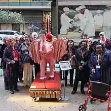 A group of volunteers stand behind a Dumbo the Elephant costume on display.