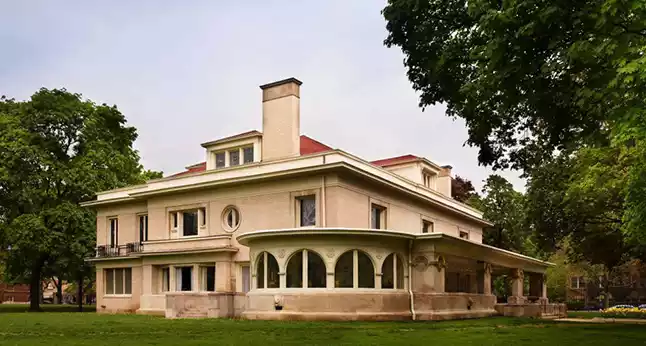 The historic Oak Park Conservatory, a large, light-colored house with a red roof and a distinctive arched porch, surrounded