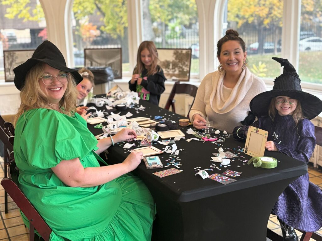 moms and daughters dressed in witch hats do a craft on the porch at pleasant home