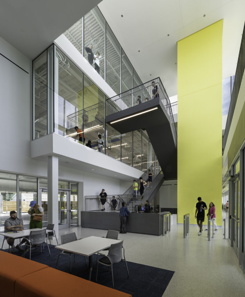 Modern building interior with people on stairs and balconies, featuring a bright yellow accent wall and open-plan design.