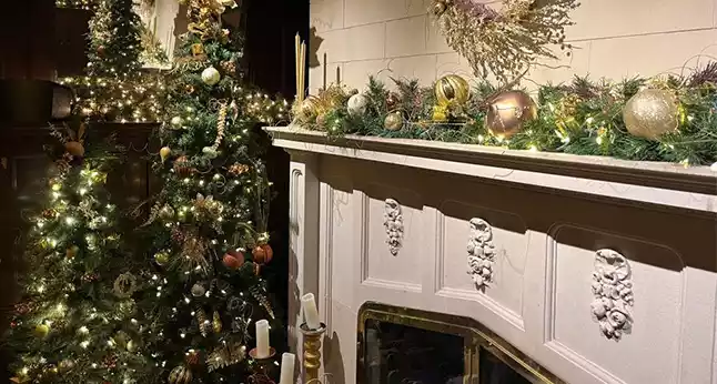 Cheney Mansion decorated for the holidays with two Christmas trees and a garland-adorned mantelpiece.