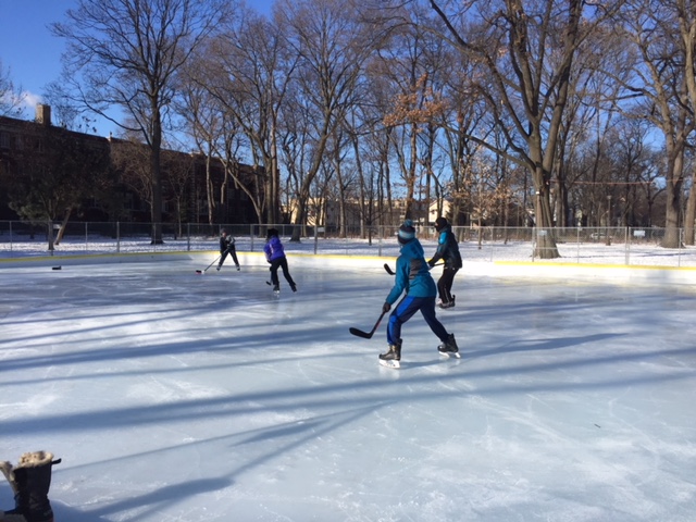 Children playing hockey on an outdoor ice rink on a sunny winter day.