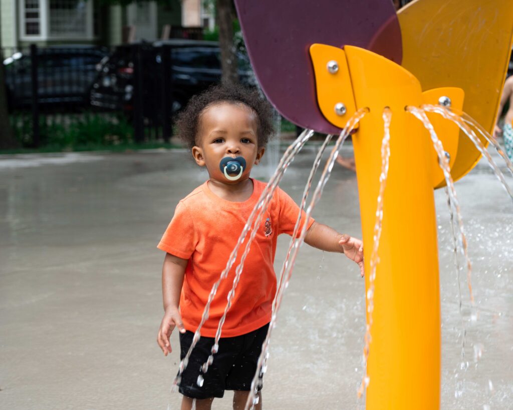 boy with pacifier stands by yellow water structure