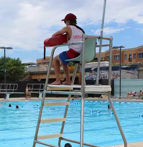 Lifeguard monitoring swimmers from an elevated chair at an outdoor pool.
