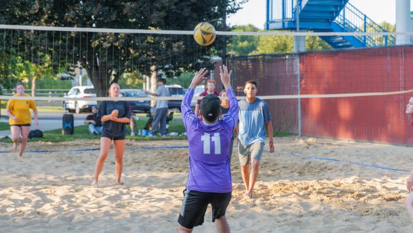 a man in a purple jersey prepares to set a volleyball