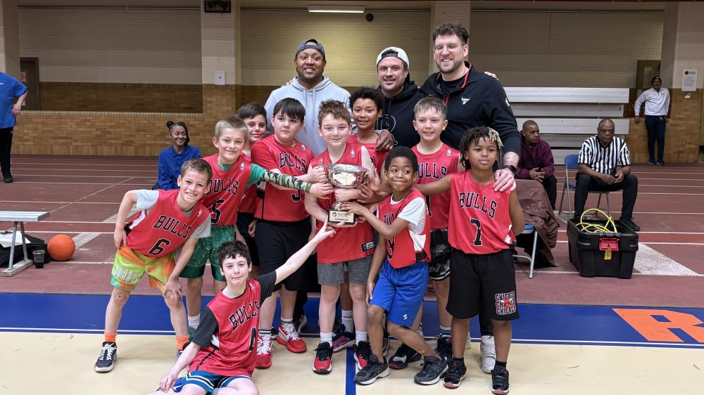 a basketball team and three volunteer coaches hold up their championship trophy