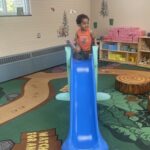 young child gets ready to go down blue slide