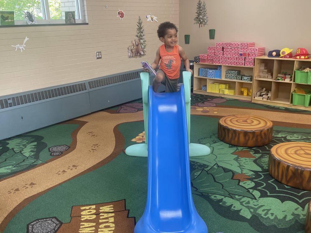 young child gets ready to go down blue slide