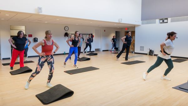 a group of people work out in a large room with yoga mats on tan hardwood floors